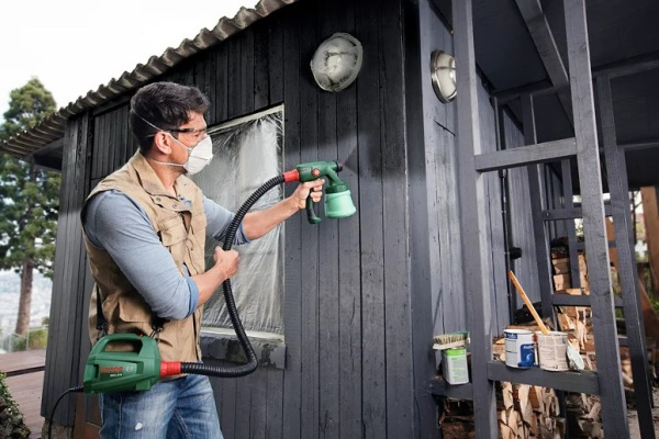Hombre pintando la caseta de su jardín con una pistola eléctrica de pintura