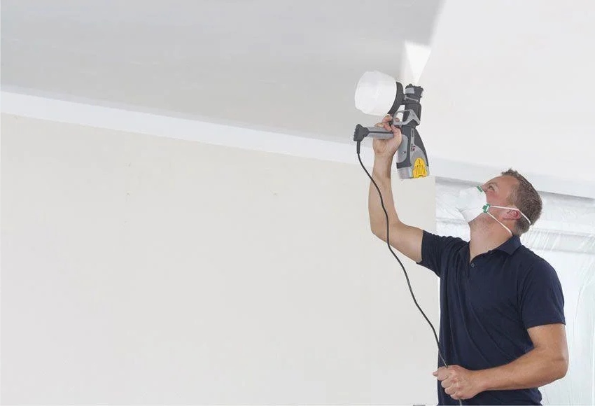 hombre pintando el techo de su casa con una pistola eléctrica para pintar